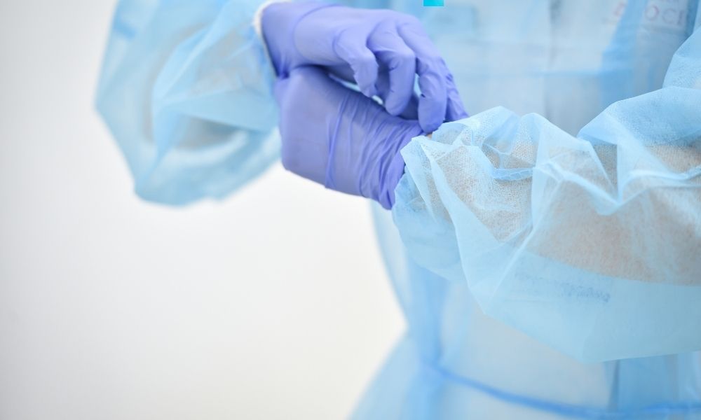 Ein Mann mit hellblauem Schutz-Overall zieht lila-blassblaue Einweghandschuhe an.