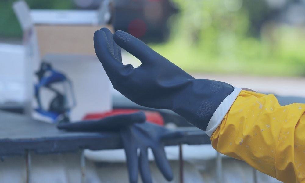 Mit schwarzem Gummi überzogene Nylonhandschuhe. Die Person trägt außerdem einen gelben Regenmantel.